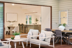 Outdoor Living Area Overlooking the Kitchen A cozy outdoor living space with comfortable seating and a modern dining table, offering a view into a stylish kitchen through an open sliding door.
